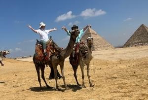 A man riding on the back of two camel.